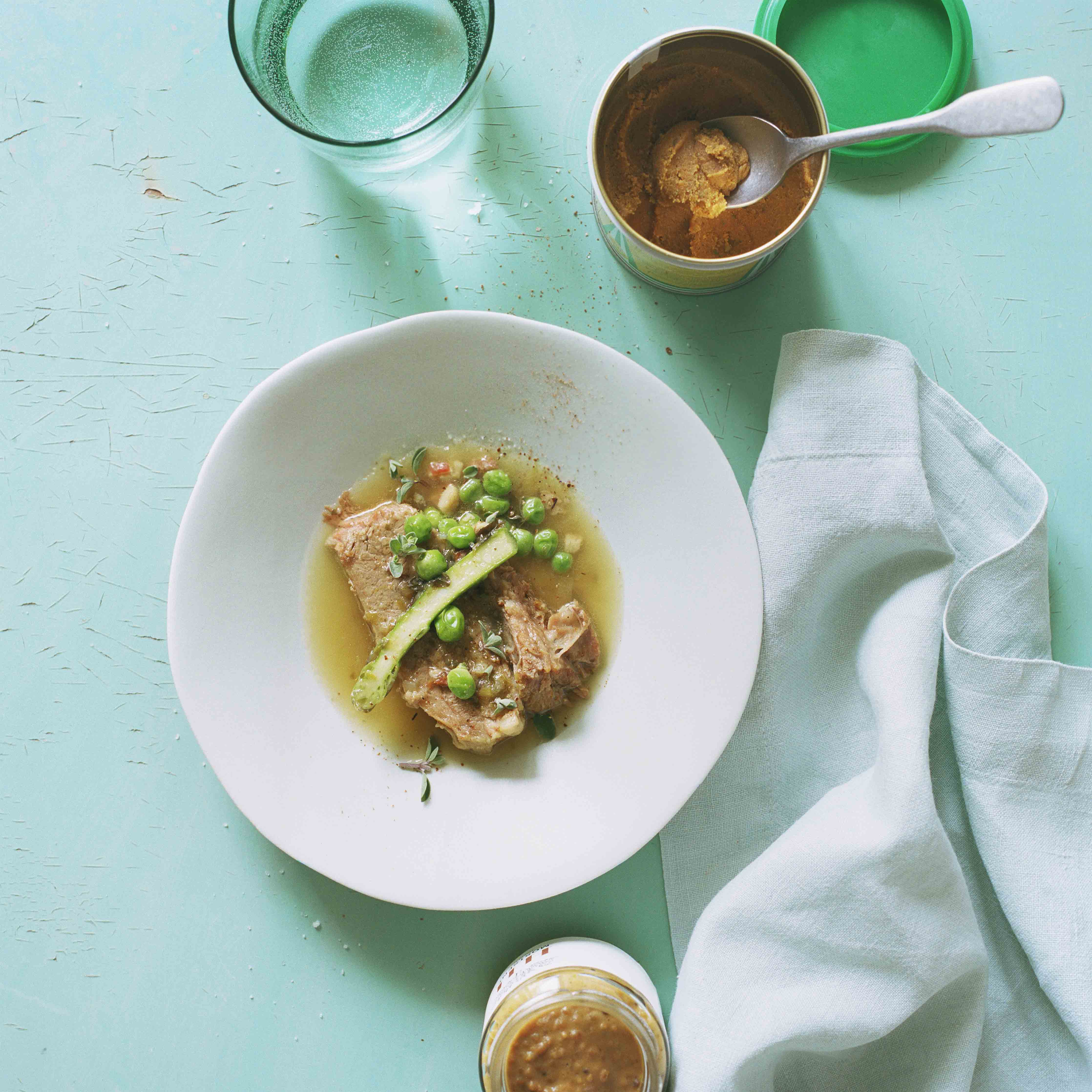 Das Hauptgericht Pot-au-feu mit Erbsen und Spargeln auf einem türkisfarbenen Tisch und einer offenen Dose Dowa Gemüsebouillon