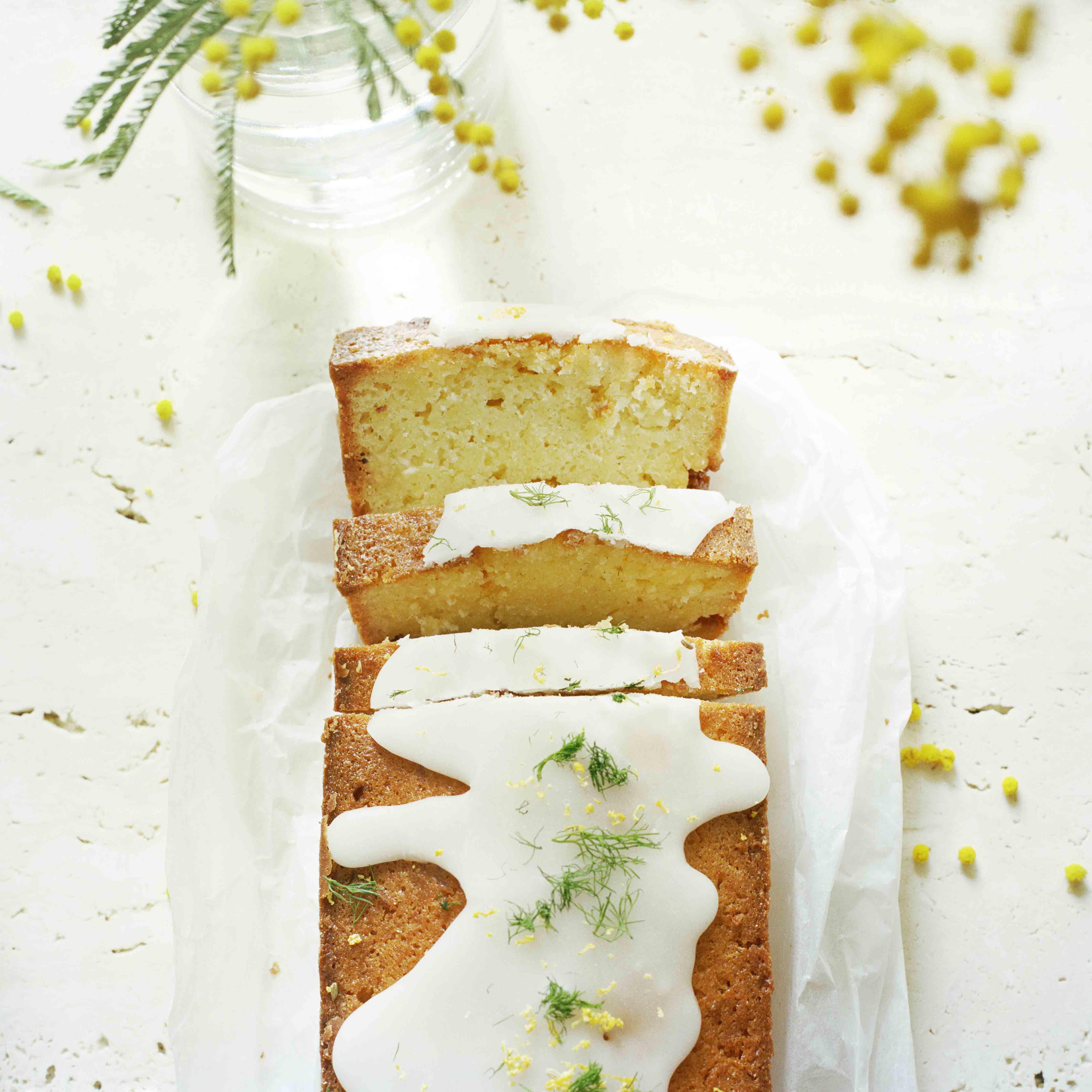Ein angeschnittener Fenchel-Pastis-Cake mit weisser Schokolade auf porösem Marmor und mit Fenchelkraut garniert