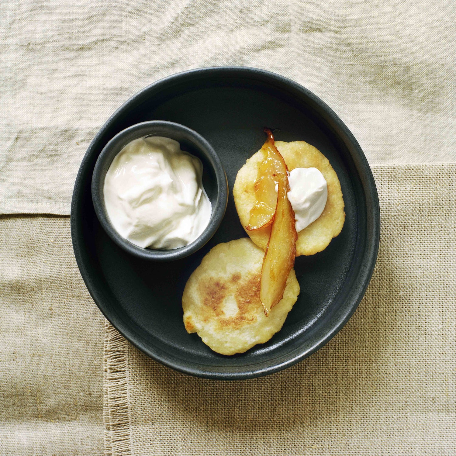 Das Dessert Kartoffelküchlein mit karamellisierten Birnen und Sauerrahm in einem dunklen Porzellanteller