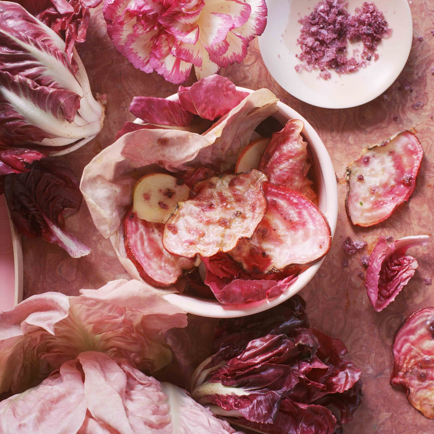 Die Vorspeise Radichhio mit Randenchips garniert mit rosa Blumen auf rosa Marmorgrund