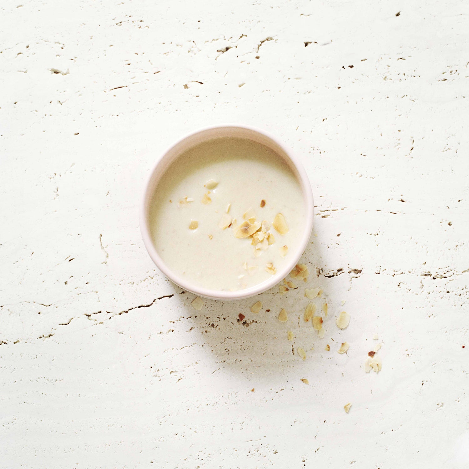 Eine Schale mit Topinambursuppe mit Mandeln als Vorspeise präsentiert auf hellem Stein