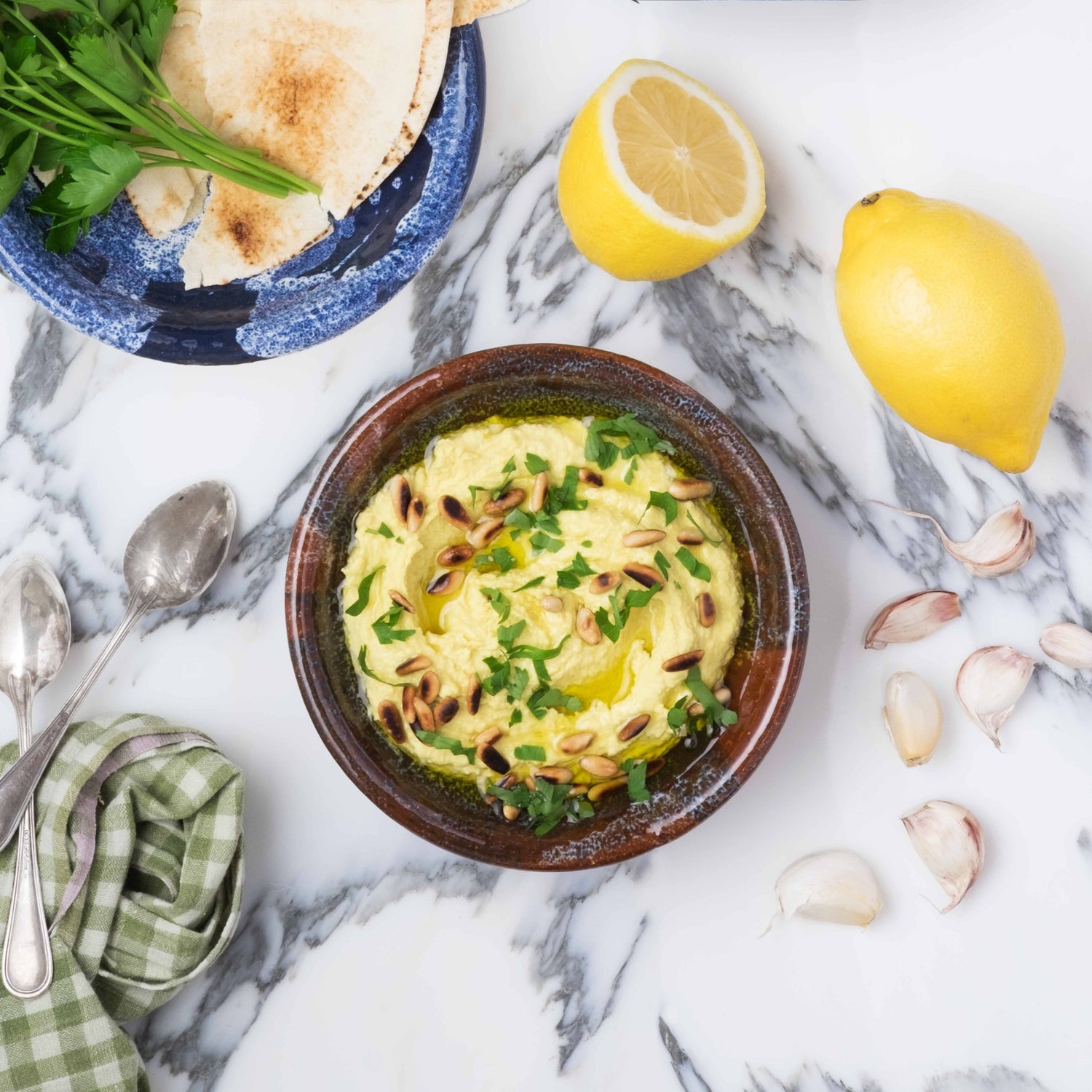 Hummus mit garniert mit Pinienkerne und Petersilie neben Zitronenhälften und Knoblauchzehen
