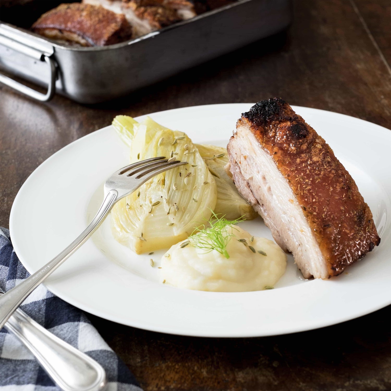 Eine Tranche geschmorter Schweinebauch mit Fenchelhälfte und Püree auf weissem Teller