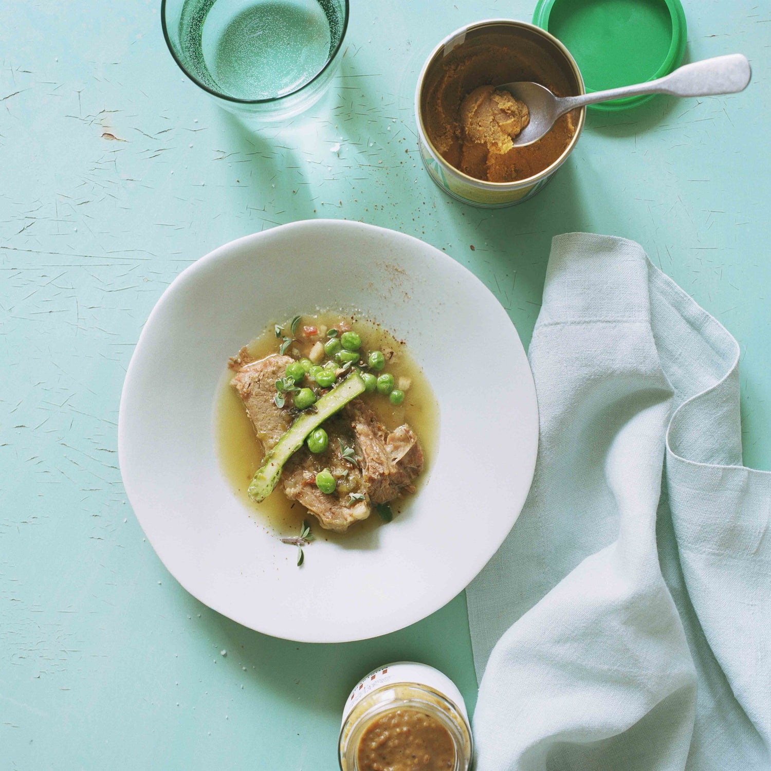 Das Hauptgericht Pot-au-feu mit Erbsen und Spargeln auf einem türkisfarbenen Tisch und einer offenen Dose Dowa Gemüsebouillon