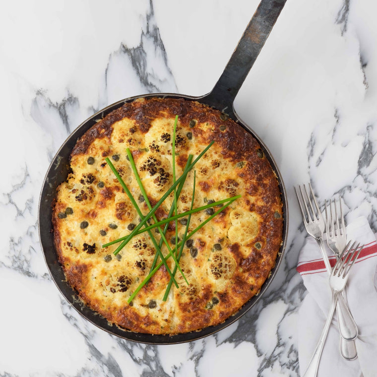 Mit Scamorza überbackener Blumenkohl in einer Bratpfanne aus Eisen garniert mit Schnittlauch