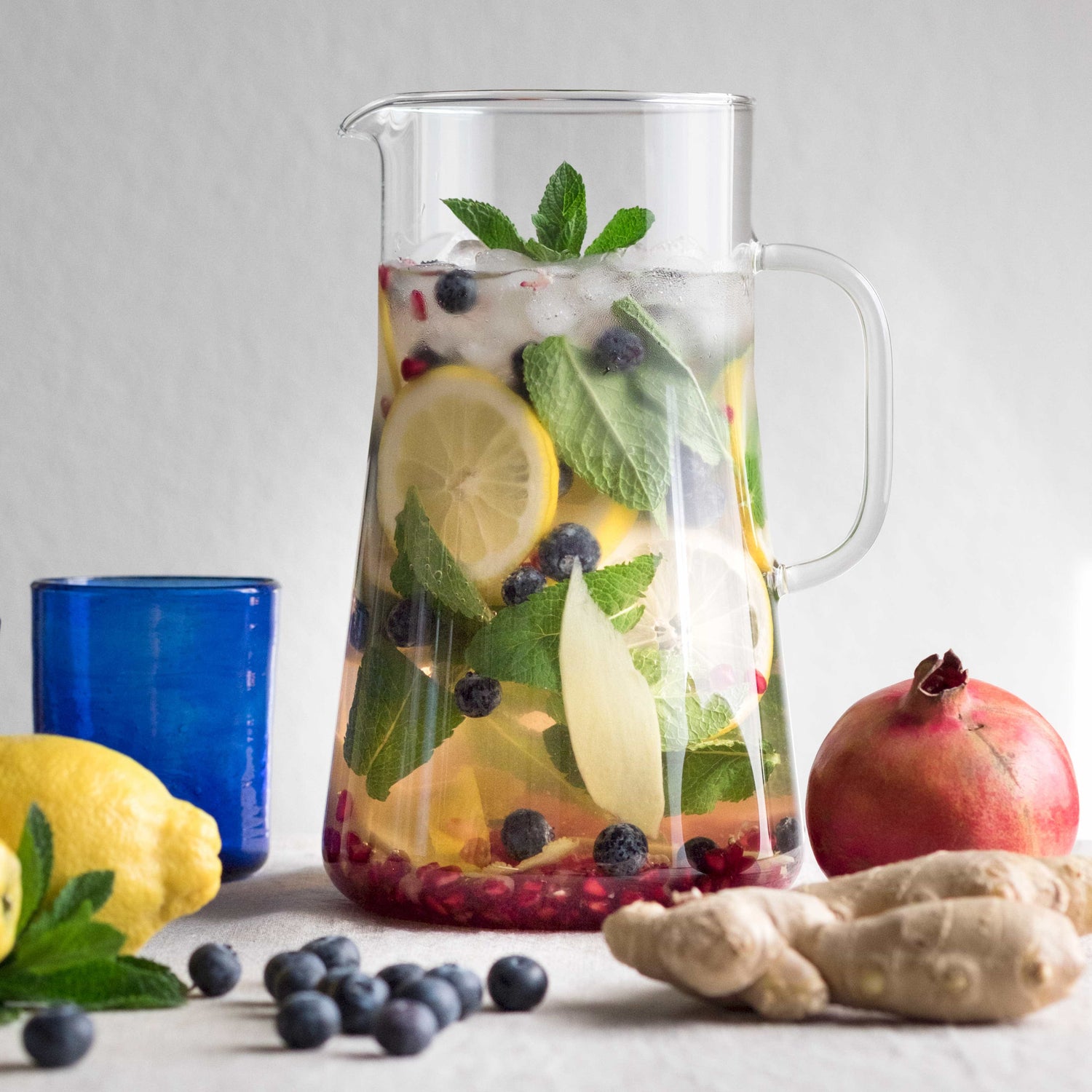 Glaskrug mit Limonade, Zitronenscheiben, grünen Minzeblättern und Blaubeeren