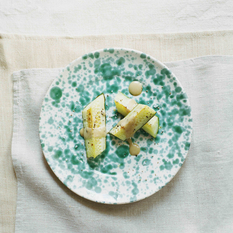 Gebratene Gurke an Sesamsauce auf einem marmorierten Vorspeisenteller der wiederum auf Küchentüchern aus Leinen liegt 
