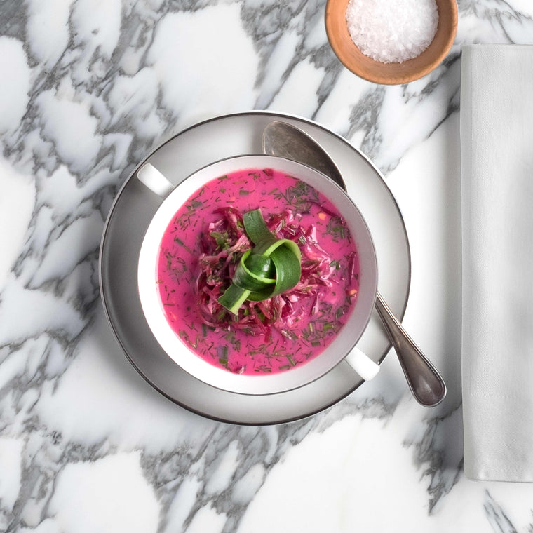 Rosafarbene Randensuppe mit Gurkendekoration auf weisser Marmorplatte
