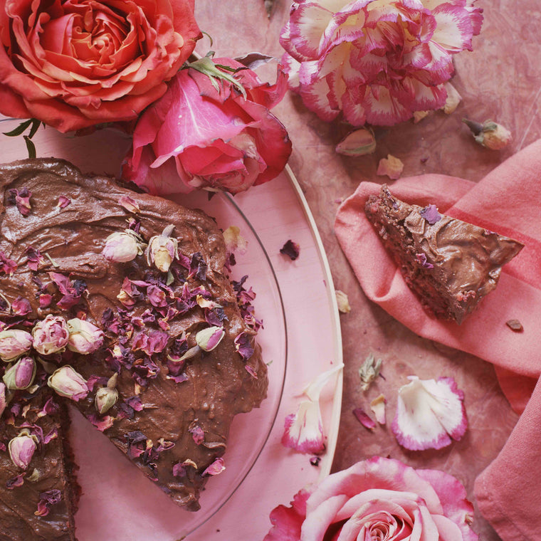 Randenkuchen mit Schokolade auf rosa Untergrund dekoriert mit Rosen und Blüten