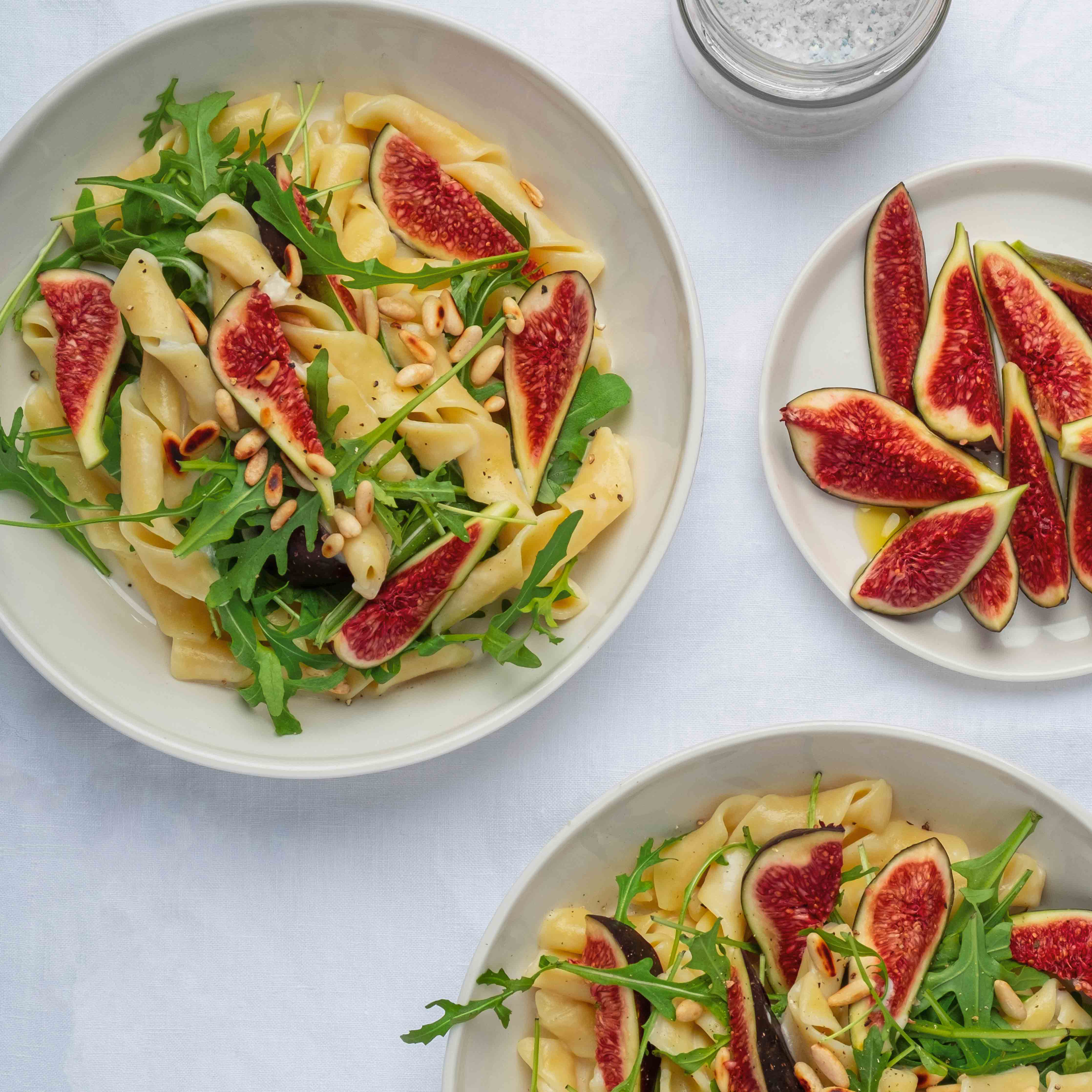 Zwei weisse Teller gefüllt mit Pasta, Feigenspalten und grünem Rucola
