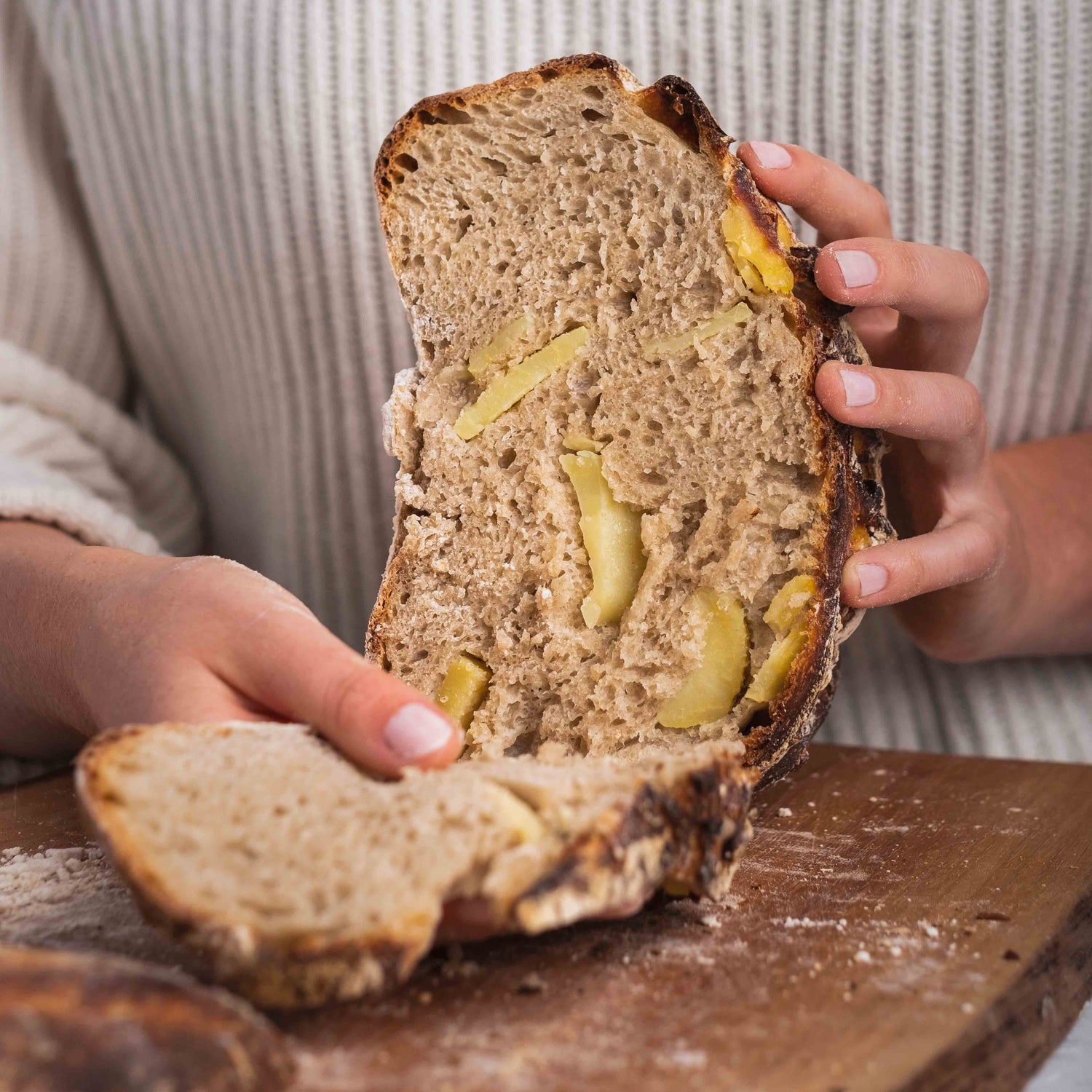 Zwei Hände halten ein aufgeschnittenes Kartoffelbrot über einem Holzbrett 
