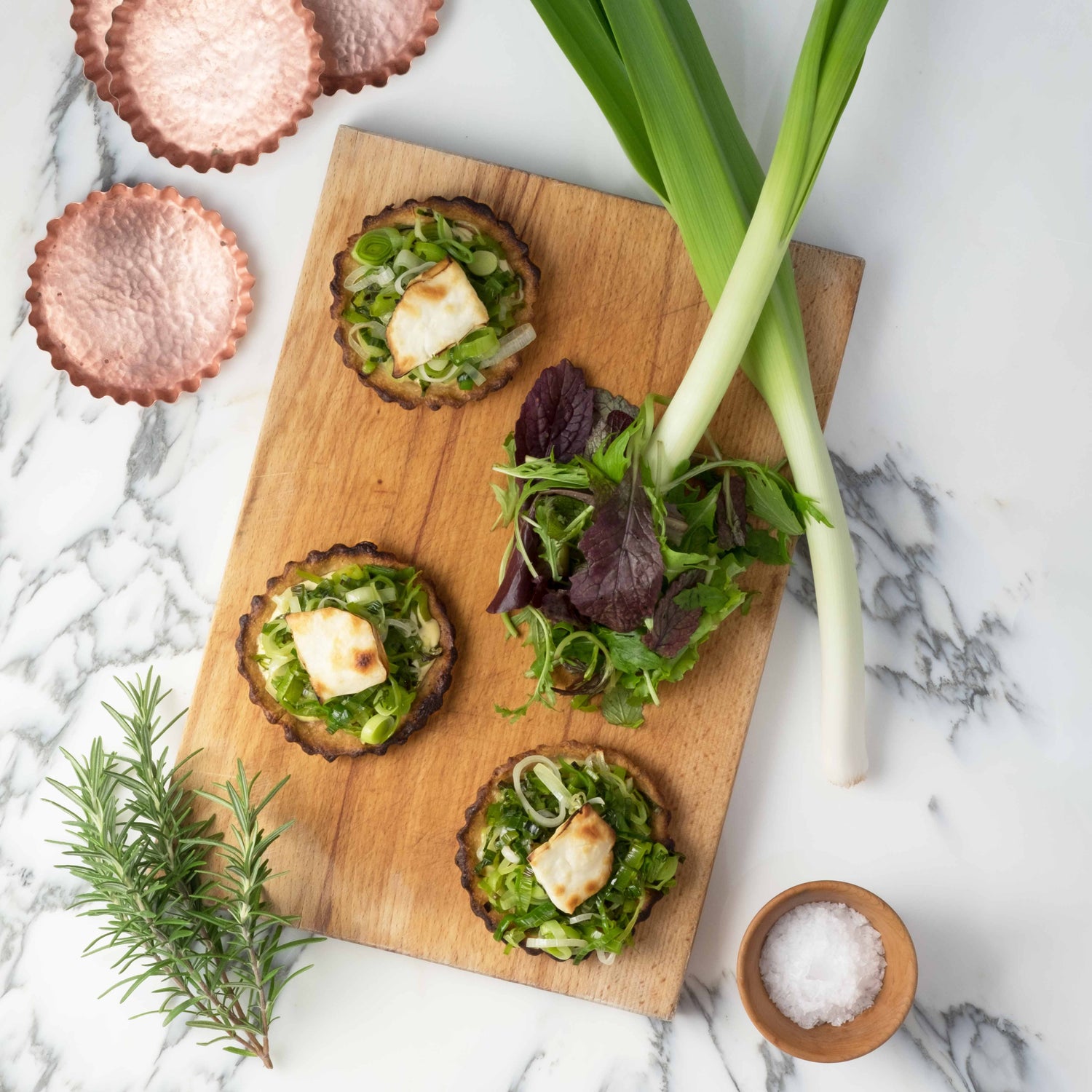Lauchküchlein mit Rosmarinzweig und Ziegenkäse auf rechteckigem Holzbrett