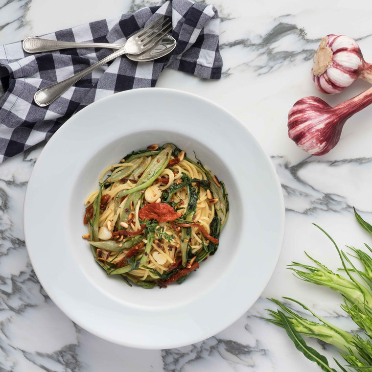 Weisser Teller mit Spaghetti alla Catalogna auf Marmortisch mit Knoblauch und grünem Gemüse arrangiert