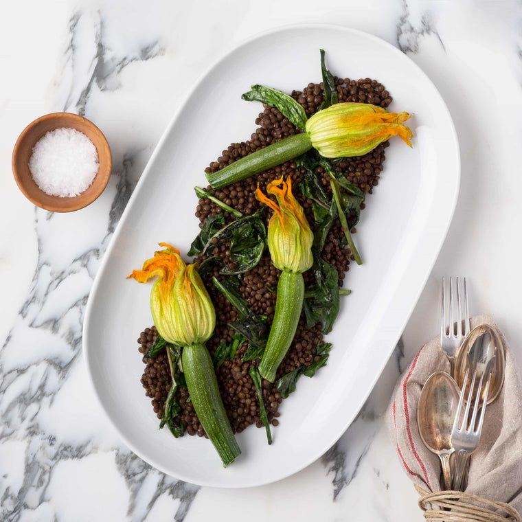 Weisse Porzellanplatte mit Linsensalat und orangefarbenen Zucchiniblüten darauf