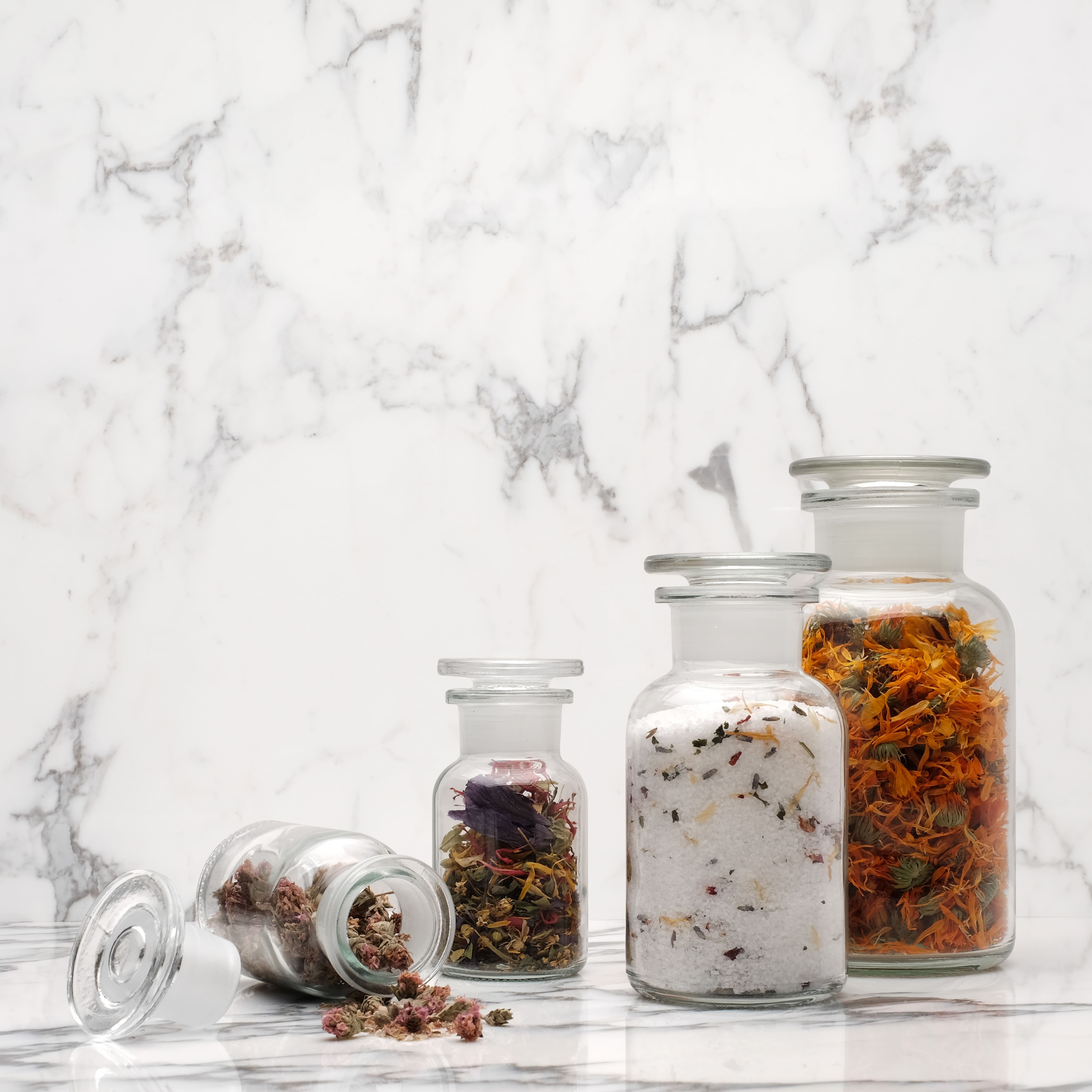 mood: Moodbild der gefüllten Apothekerflaschen mit bunten Kräutern und Blumen vor weissem Marmor