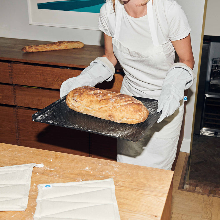 Bäckerin trägt die Veark Ofenhandschuhe um sicher ein Backblech aus dem Ofen zu nehmen